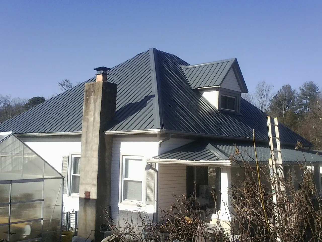 Dark blue standing seam metal roof on a white farmhouse with dormer — Slate & Tile Roof Repair by Roofing Brothers in Ririe
