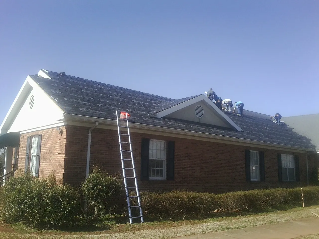 Crew tearing shingles off a brick ranch roof with a ladder set — Emergency Roof Repair work by our crew in Ririe