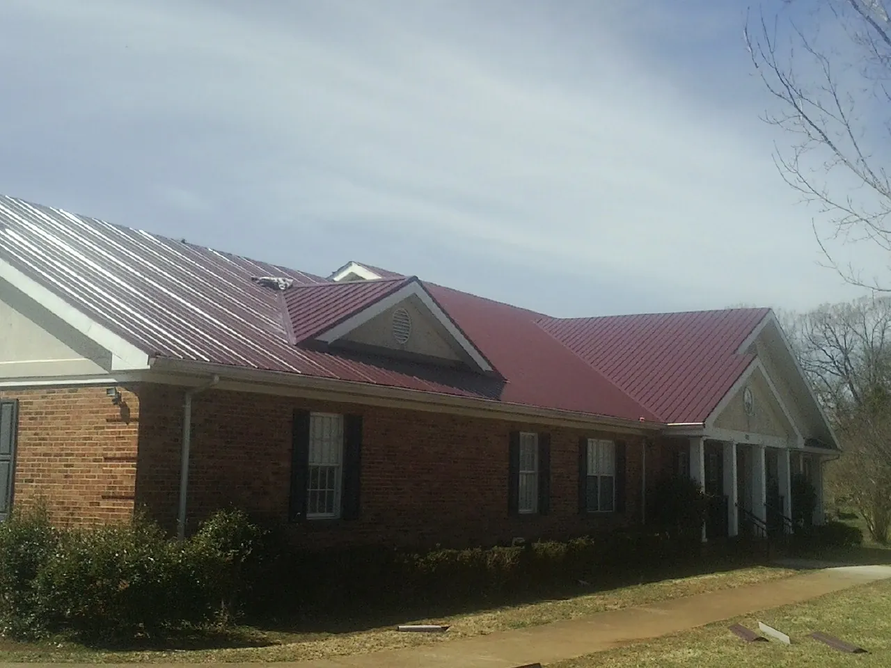Red metal roof with gabled entries on a long brick building, from a Hail Damage Roof Repair job in Ririe