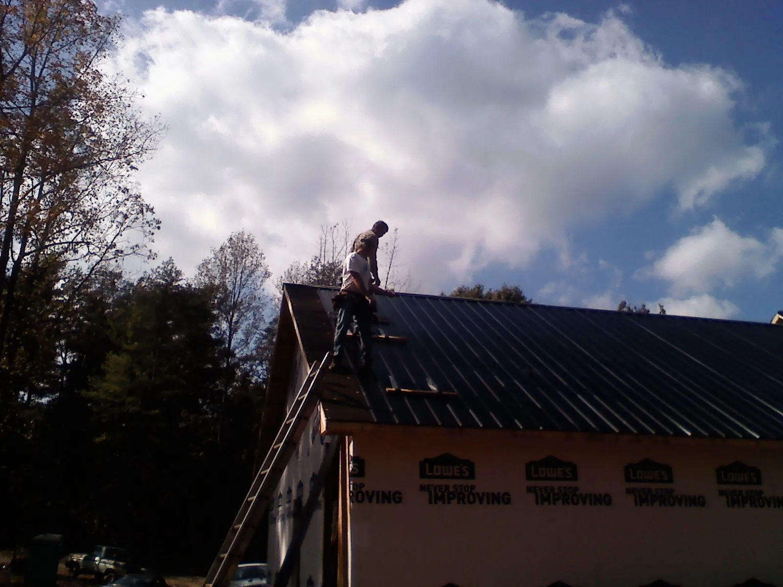Roofer fastening dark metal panels high against a cloudy sky, from a Roof Inspection job in Ririe